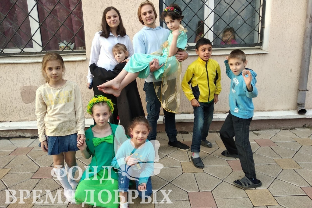 Девочка на руках у парня, фотография детей и волонтеров возле здания1602323227